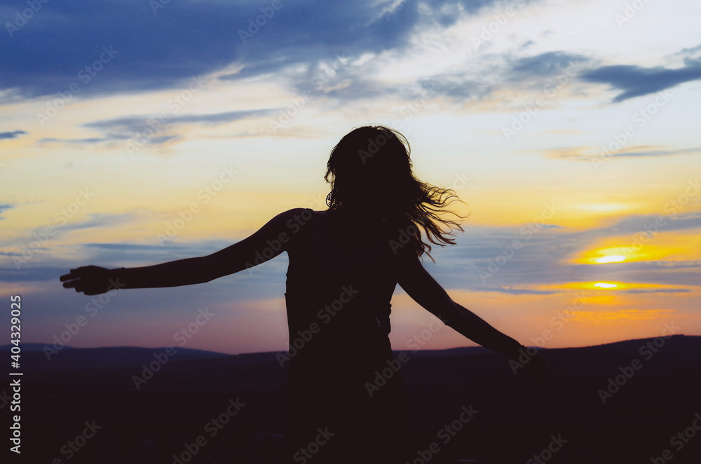 Silhouette of a woman with arms outstretched and hair in the wind in sunset. Concept: freedom, zen, relaxation