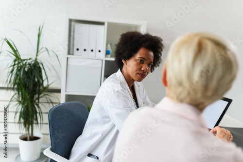 A female black ethnicity doctor sits at her office and talking with elderly female patient
