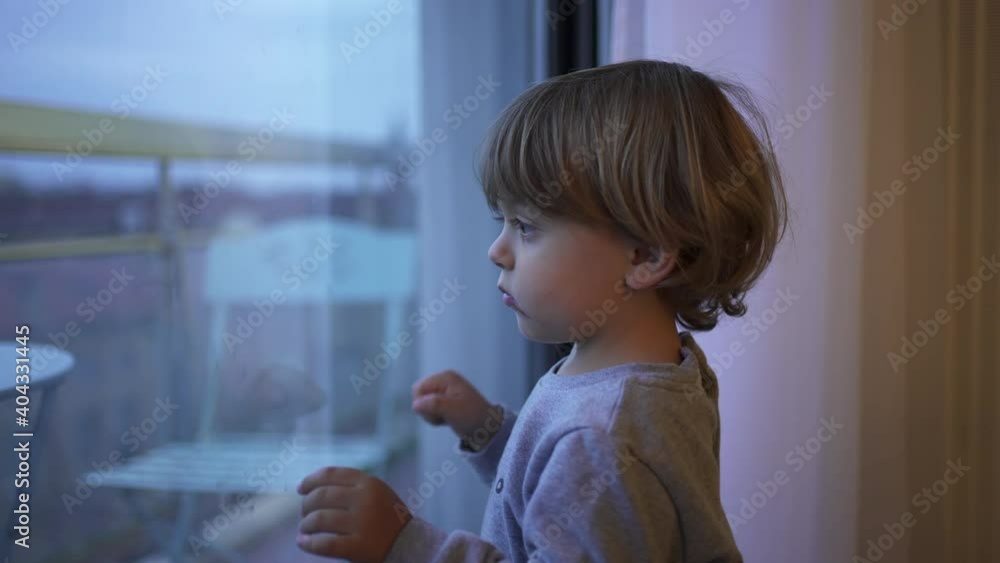 Bored little toddler child wanting to outside stuck at home. Baby standing by window looking out Bored little toddler child wanting to outside stuck at home. Baby standing by window looking out