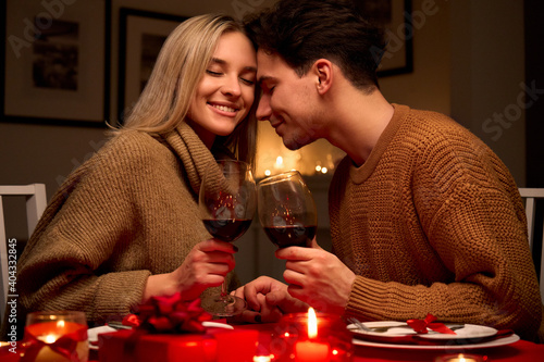 Happy young couple in love clinking glasses drinking red wine having romantic dinner date celebrating Valentines day evening or enjoying anniversary sitting at table at home or in restaurant. photo