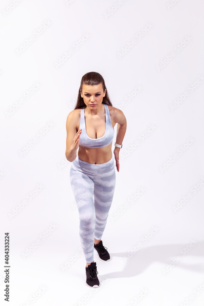 Full length active persistent woman in white sportswear ready to run, standing on start position, sprint. Indoor studio shot isolated on gray background Full length active persistent woman in white sportswear ready to run, standing on start position, sprint. Indoor studio shot isolated on gray background
