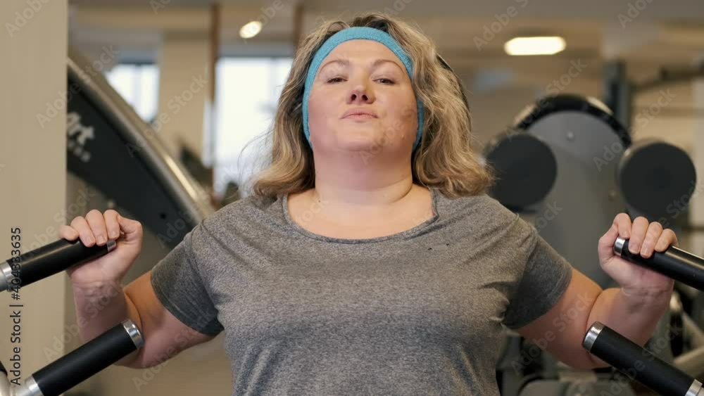 Overweight woman exercising on shoulder press machine in fitness center. Excess body weight. Overweight woman exercising on shoulder press machine in fitness center. Excess body weight.