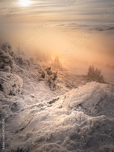 Scenic landscape with a view from a mounatin range to the valley filled with low clouds and fog during temperature inversion,snow,rime,clouds,spruce trees,rock.Jeseniky mountains.Czech republic. .