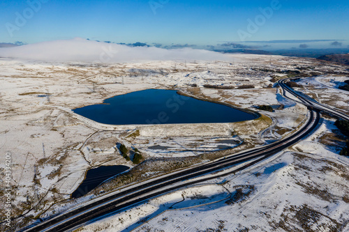 Aerial view of a large reservoir next to a major dual carriageway on a snowy day