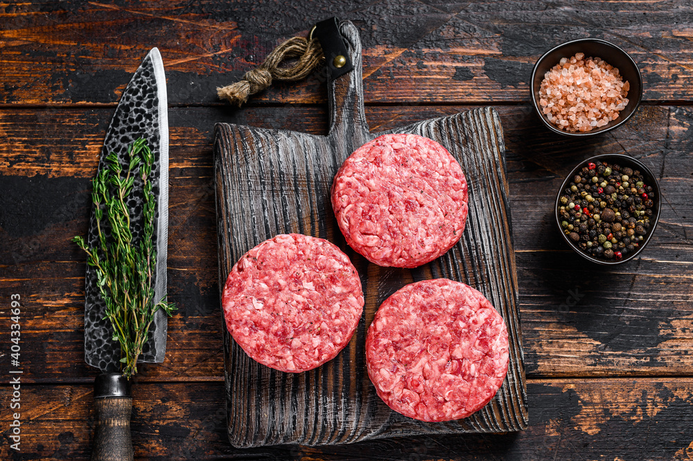 Raw steak burgers patties with ground beef and thyme on a wooden cutting board. Dark Wooden background. Top view