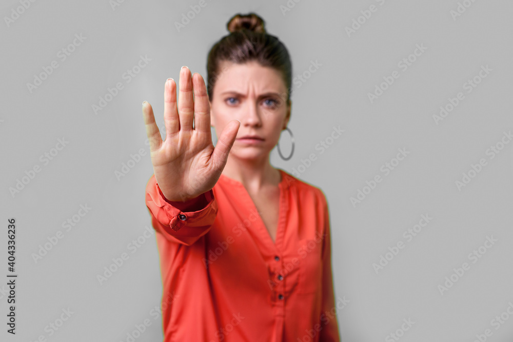 Stop, no! Portrait of angry or worried young woman with bun hairstyle, big earrings and in red blouse frowning gesturing caution to camera, prohibition. indoor studio shot isolated on gray background Stop, no! Portrait of angry or worried young woman with bun hairstyle, big earrings and in red blouse frowning gesturing caution to camera, prohibition. indoor studio shot isolated on gray background