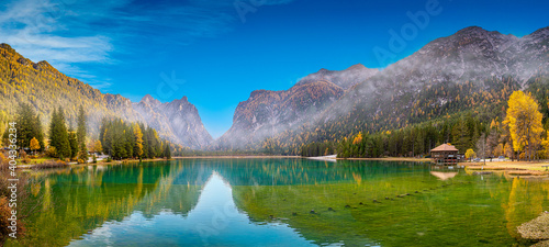 Panoramic view over the Toblacher Lake (Lago di Dobbiaco) and Dolomite mountain summits nearby in Autumn October colors at foggy morning, Dolomites, South Tyrol, Italy