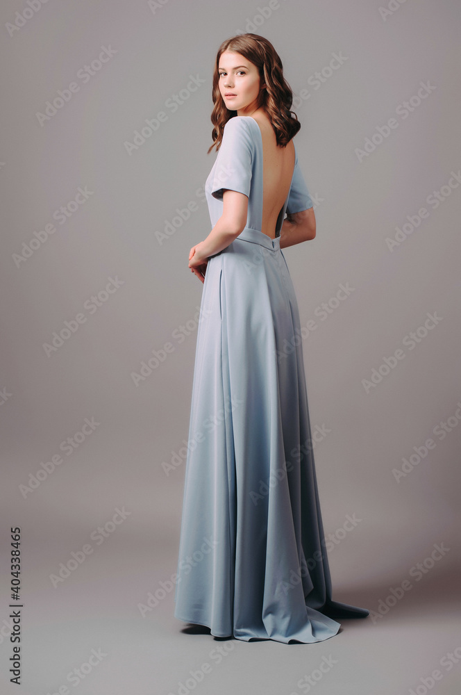Blue evening dress with back slit. Beautiful female gown. Young adult elegant lady in high heels, studio shot. Bridesmaids dress. Female fashion concept. Blue evening dress with back slit. Beautiful female gown. Young adult elegant lady in high heels, studio shot. Bridesmaids dress. Female fashion concept.
