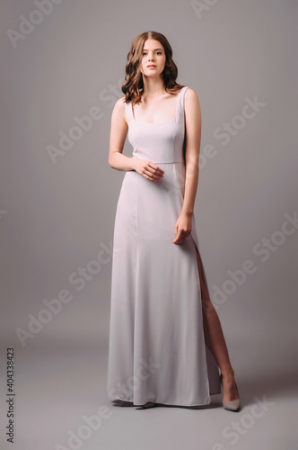 Purple evening dress with front slit. Luxury female gown. Young adult elegant lady in high heels, studio shot. Bridesmaids violet dress. Female fashion concept.