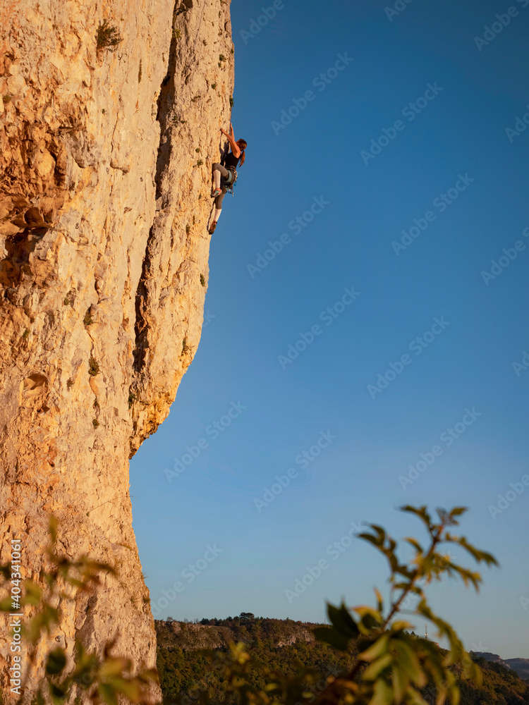 VERTICAL Woman is rock-climbing up towering rocky wall on a sunny summer evening