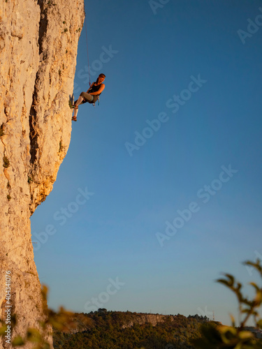 VERTICAL: Fit young woman stops and looks back at sunset while rock climbing.