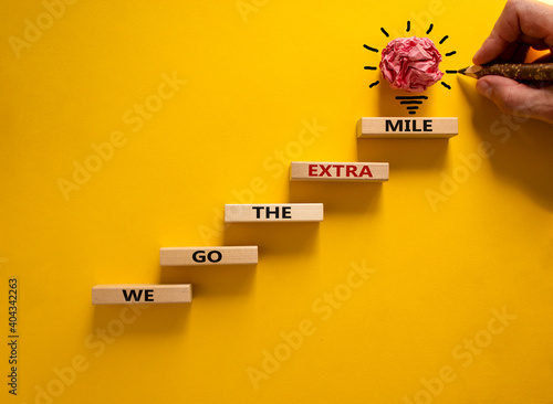 We go the extra mile symbol. Wood blocks stacking as step stair on beautiful yellow background, copy space. Male hand, light bulb. Words 'We go the extra mile'. Business and go the extra mile concept. photo