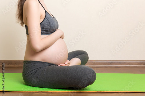 beautiful young pregnant woman sitting on mat in yoga pose at the home. Pregnancy Yoga and Fitness concept at coronavirus time
