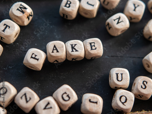 The word  FAKE  made from letter beads on a black wooden background