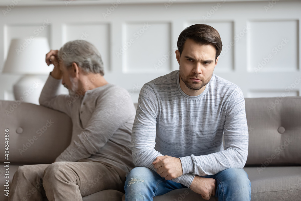 Angry stubborn millennial adult man and mature father avoid talking after family fight. Unhappy elderly dad and grownup son ignore each other sit back to back after quarrel. Generation gap concept.