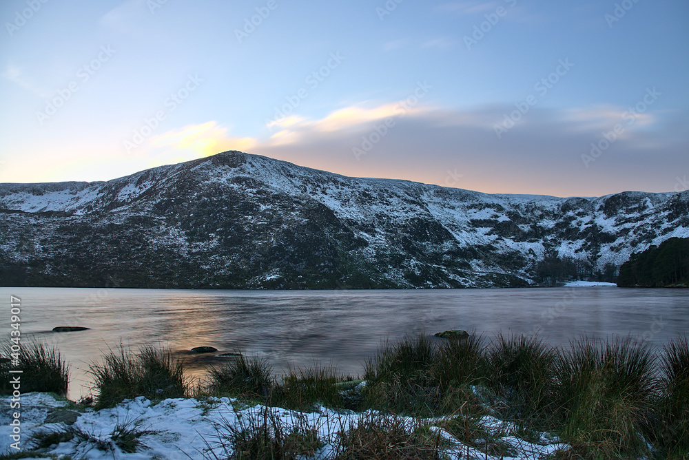 Stunning sunset above snowy Eagles Crag peak and Lough Bray Lower lake in cold winter tones, Co. Wicklow, Ireland. Winter weather in Ireland. Climate. Long exposure