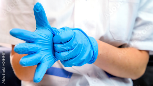 Doctor or nurse putting on blue nitrile surgical gloves, professional medical safety and hygiene for medical exames or protection against coronovirus
