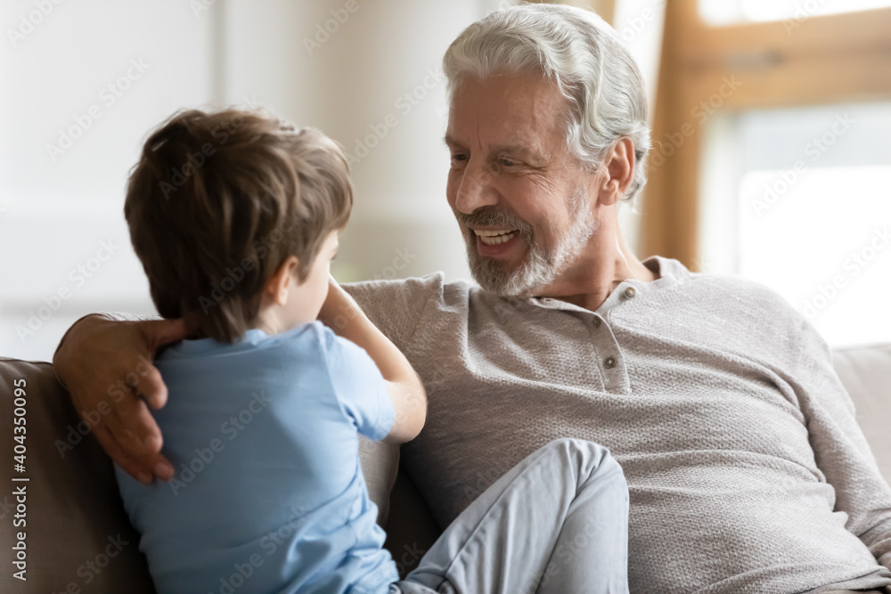Happy old 70s Caucasian grandfather sit relax at home talk with cute little grandson. Smiling mature elderly grandparent share secrets speak chat with small boy child, enjoy weekend together. Happy old 70s Caucasian grandfather sit relax at home talk with cute little grandson. Smiling mature elderly grandparent share secrets speak chat with small boy child, enjoy weekend together.