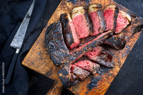 Traditional barbecue dry aged wagyu t-bone beef steak bistecca alla Fiorentina sliced and served with black salt as top view on an old rustic wooden board
