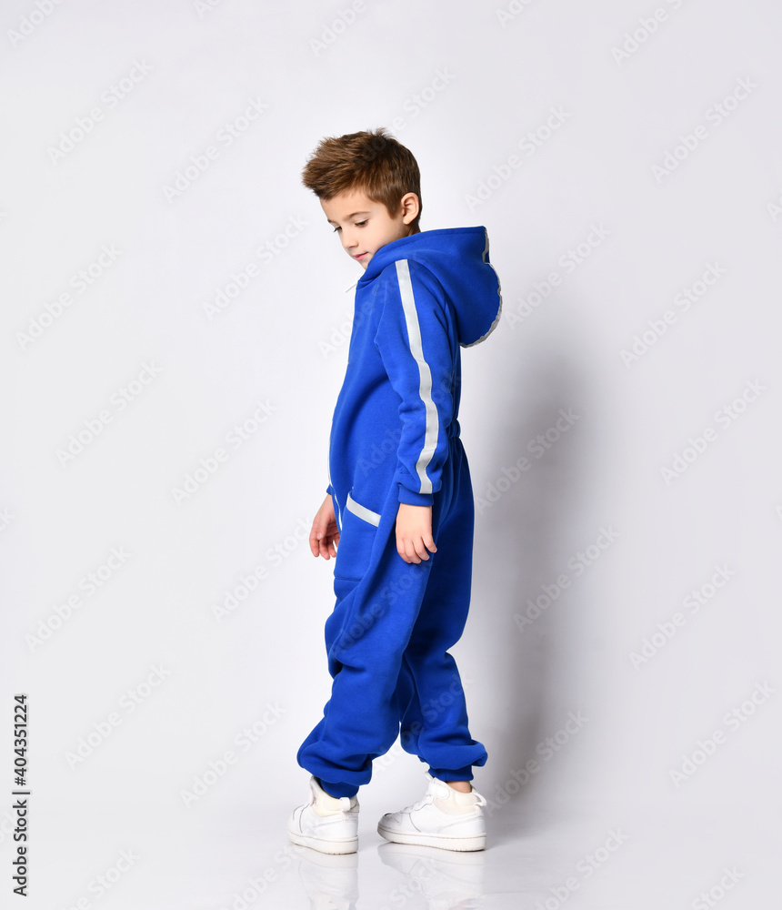 modern boy in warm blue jumpsuit and white sneakers posing for the camera against the background of a studio wall. Sports fashion clothing modern boy in warm blue jumpsuit and white sneakers posing for the camera against the background of a studio wall. Sports fashion clothing