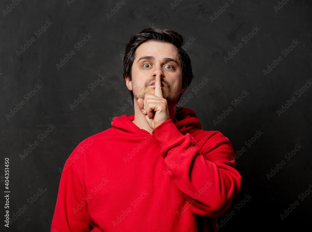 White guy in red sweatshirt show quiet gesture on dark background White guy in red sweatshirt show quiet gesture on dark background