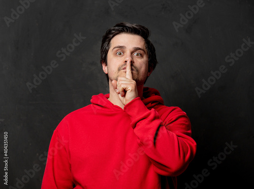 White guy in red sweatshirt show quiet gesture on dark background
