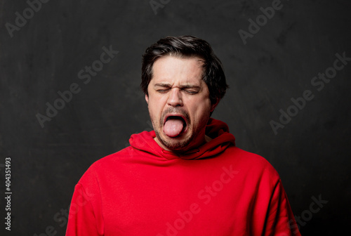 White guy in red sweatshirt show disgusting emotion on dark background