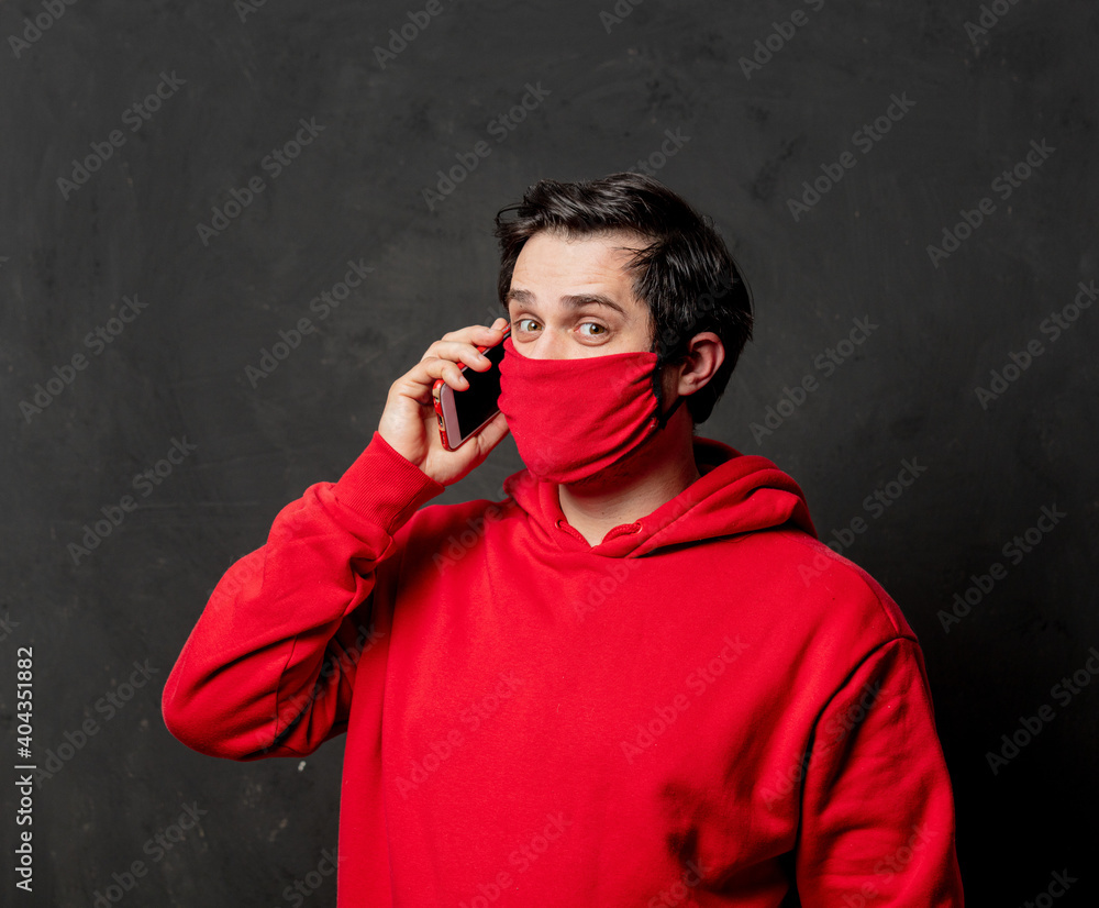 guy in red sweatshirt and face mask using mobile phone on dark background guy in red sweatshirt and face mask using mobile phone on dark background