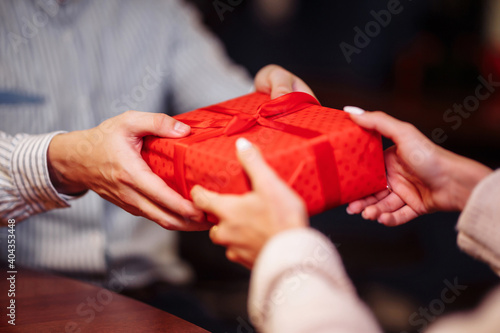 Valentine's Day concept. Close shot of man's and woman's hands presenting gifts to each other at a cafe. A young loving couple celebrating in the restaurant. New normal, winter holidays.