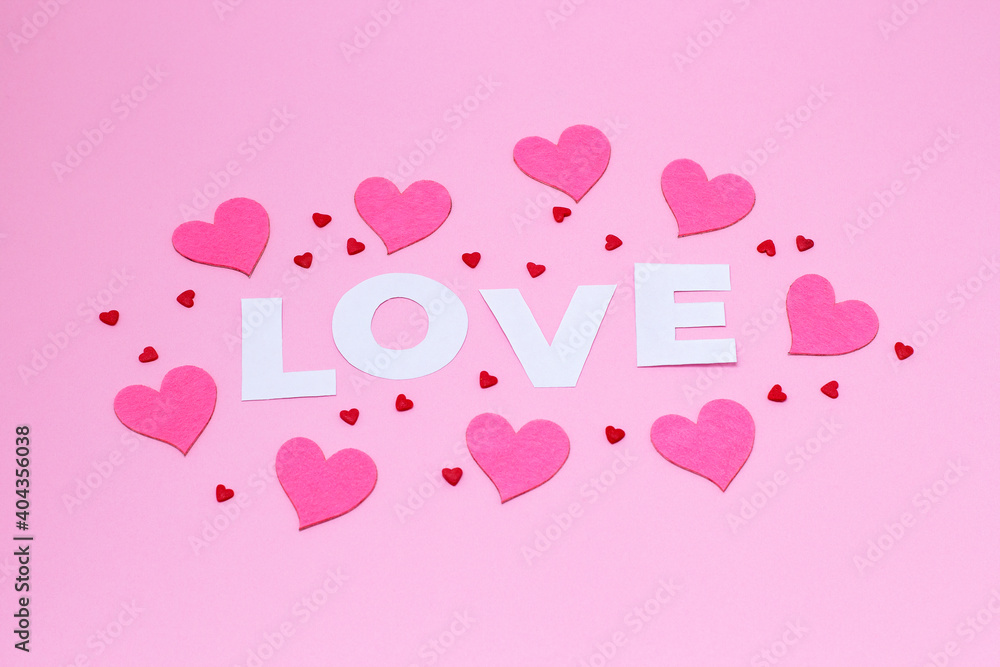 Word love in white letters with felt and sugar hearts on a trendy pink background. Valentine's Day, Mother's Day, March 8, World Women's Day holiday card concept. Flat lay.