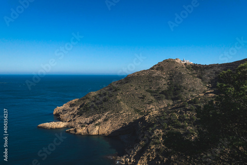 Lighthouse on rocky cliffs in deep blue ocean bay in the natural park 'Serra Gelada' in Albir, Spain