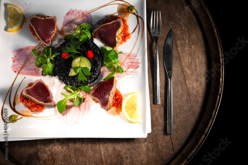 Plate with grilled tuna and black rice dish with cutlery