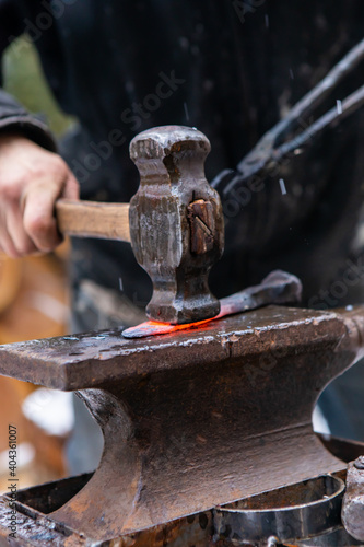 Very close up shot of a hammer flattening a red, sizzling hot rod of iron from of the forge. Blacksmith's daily work routine in an outdoor lab.
