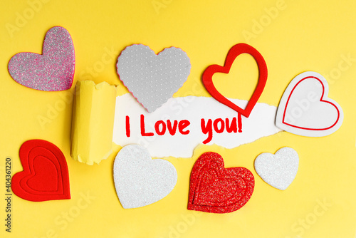 English text I love you on a torn piece of yellow paper with romantic hearts. photo
