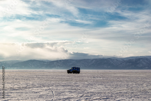 The car drives on the snow-covered ice of Lake Baikal against the background of mountains. Winter landscape. Copy space.