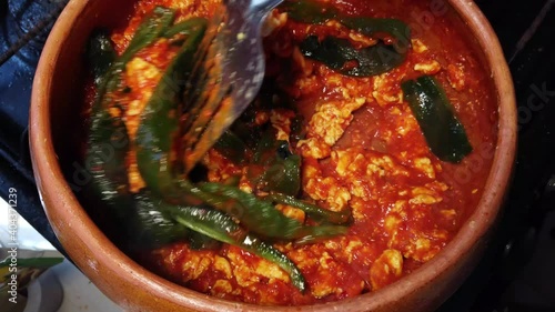 Traditional mexican eggs with red sauce and poblano pepper cooking in clay cazuela