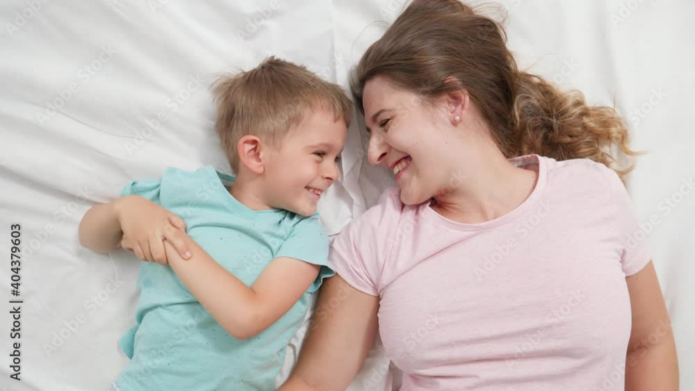 Top view portrait of cute little boy lying with young mother on bed and talking. Concept of parenting and family happiness Top view portrait of cute little boy lying with young mother on bed and talking. Concept of parenting and family happiness