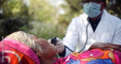 Slow-motion of medical staff in personal protective gear check examine advice about safety and hygiene to a patient sick elderly woman with face mask in red saree lying on a bed outdoors in India  
