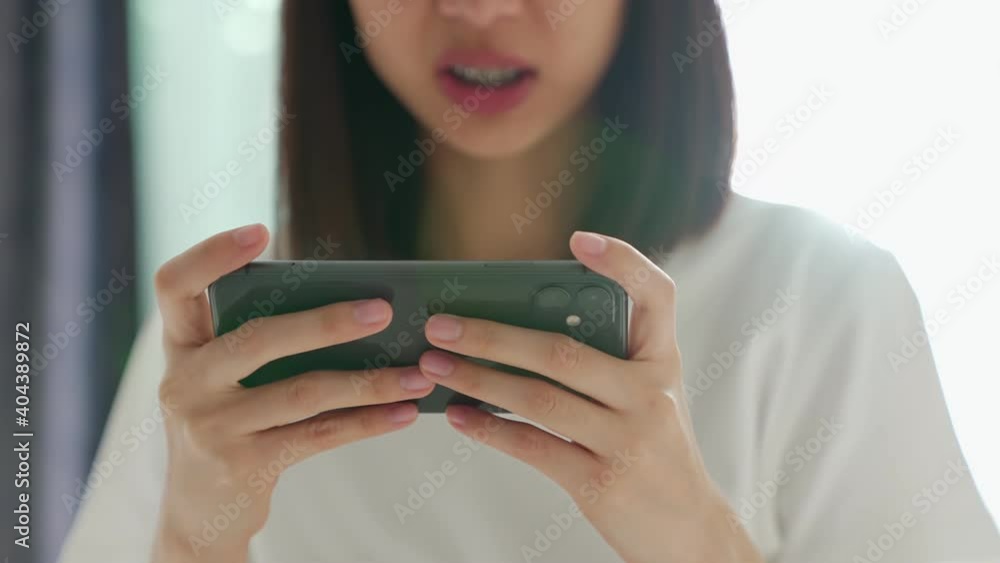 Excited young Asian woman playing games on smartphone in the living room at home. Excited young Asian woman playing games on smartphone in the living room at home.