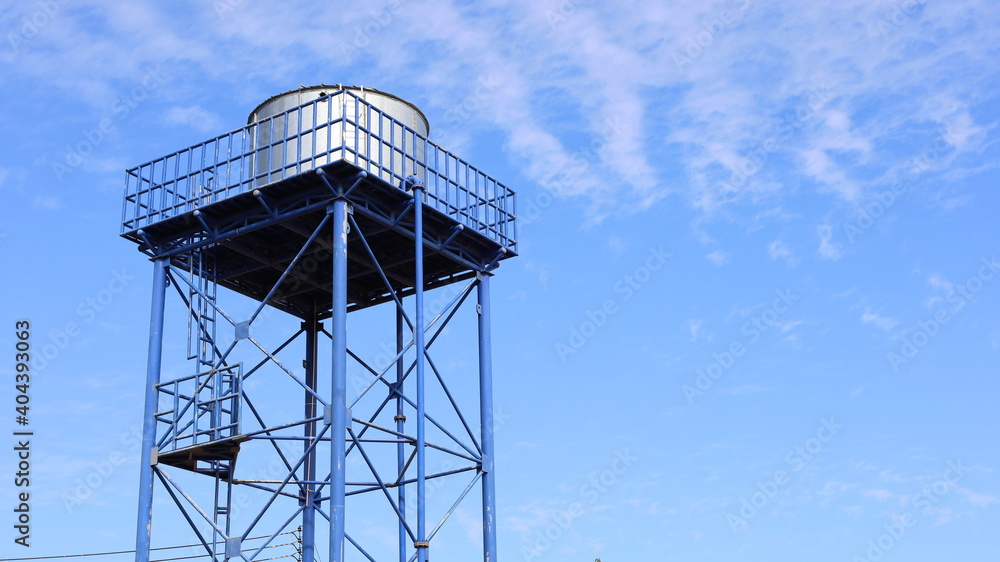 Metal water tank on the tower. Structure and storage tanks in the water supply system on a blue sky background with a copy area. Selective focus