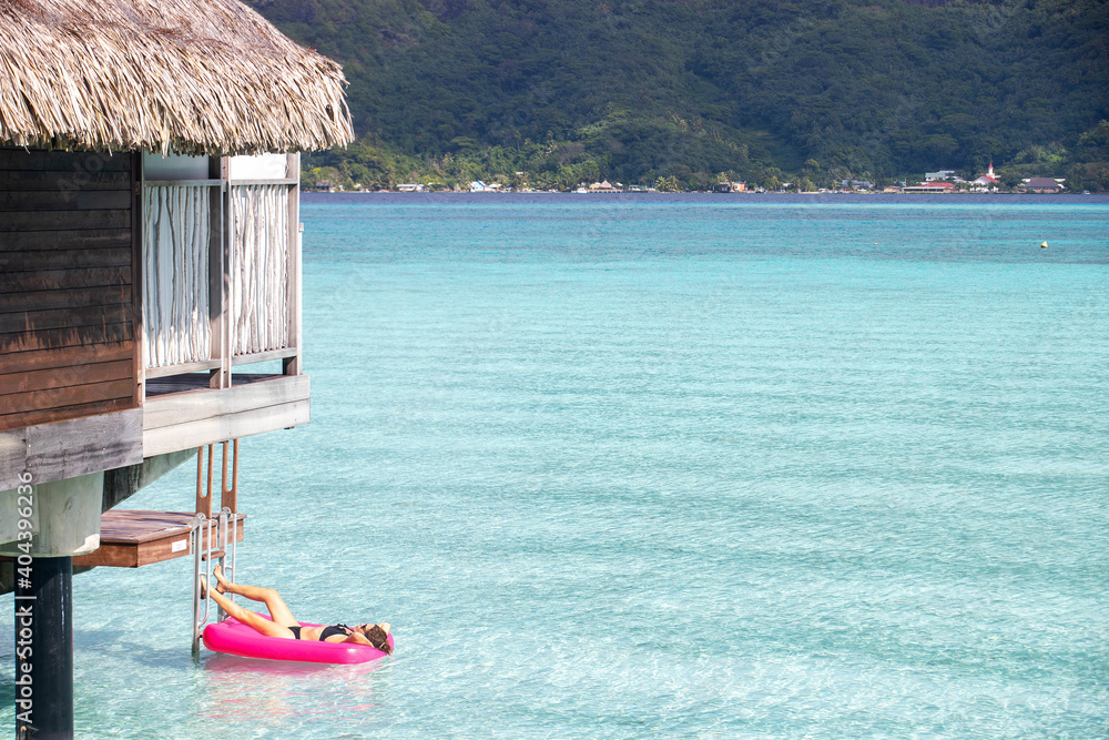 Φωτογραφία Woman relaxing on an inflatable mattress floating on a clear turquoise ocean in a tropical island lagoon next to an overwater bungalow during her summer vacation