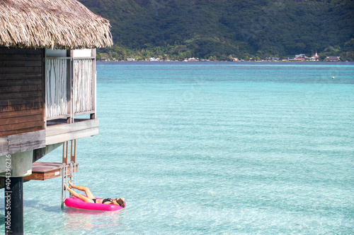 Woman relaxing on an inflatable mattress floating on a clear turquoise ocean in a tropical island lagoon next to an overwater bungalow during her summer vacation. She is tanning under the sun. photo