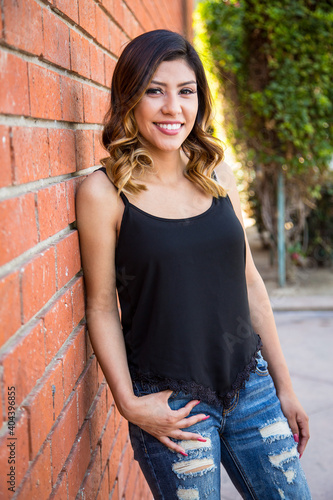 Hispanic young woman standing against a red brick wall wearing ripped jeans