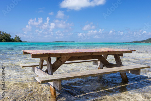 A picnic table sits in shallow, tropical ocean water on a Bora Bora motu