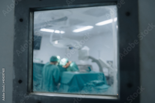 Blurred image background of medical team performing surgical operation in operating room. Look through outside operating room.