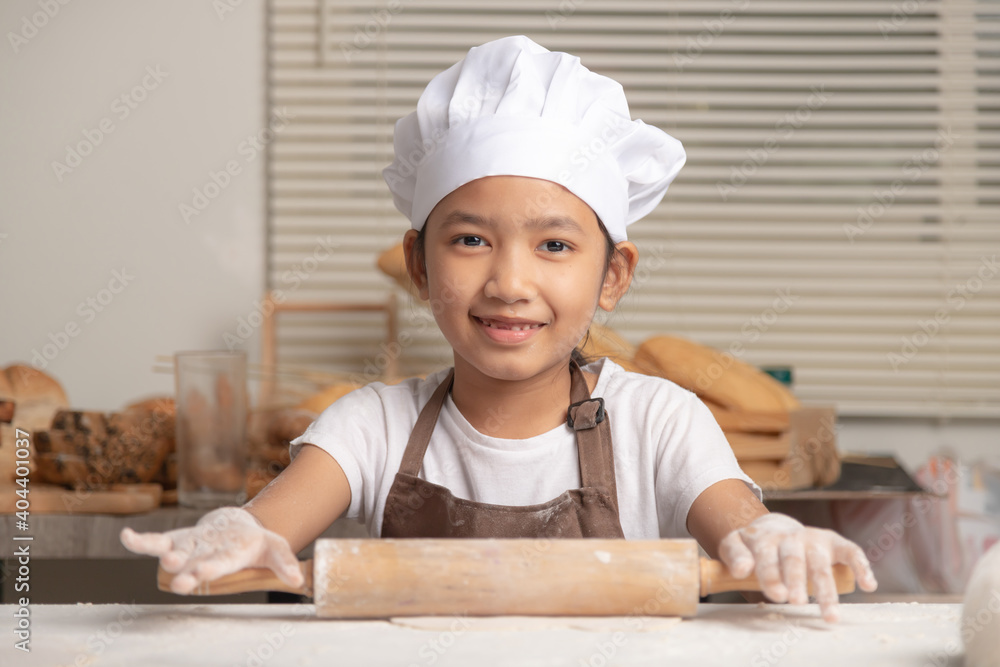 Asian little girl uses a rolling pin to knead the dough to make a homemade bakery. Asian little girl uses a rolling pin to knead the dough to make a homemade bakery.