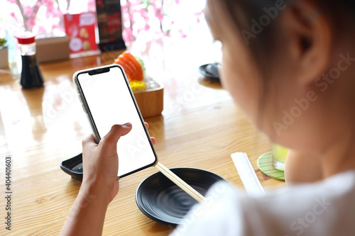 Asian woman using a smartphone in a restaurant with clipping path. A woman holding a phone with a white screen.