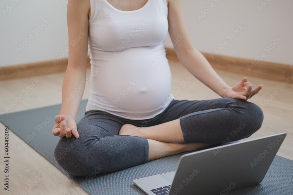 Calm pose young asian pregnant woman meditating in lotus position ,practicing yoga for maternity on laptop computer at home.