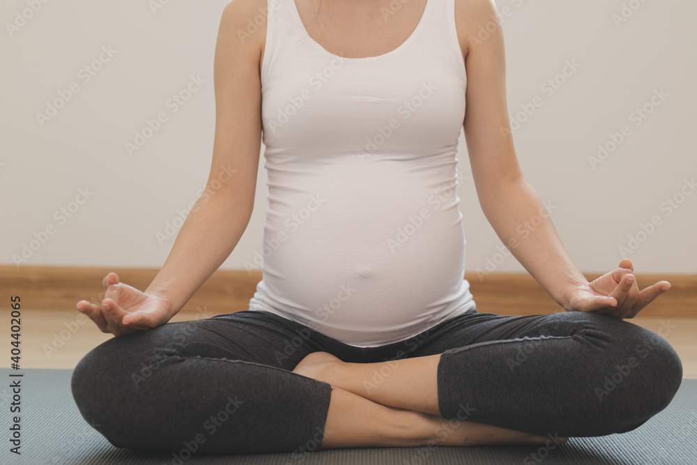 Calm pose young asian pregnant woman practice yoga in the lotus position for pregnant to meditation and exercise on mat for wellbeing while rest at home. Calm pose young asian pregnant woman practice yoga in the lotus position for pregnant to meditation and exercise on mat for wellbeing while rest at home.