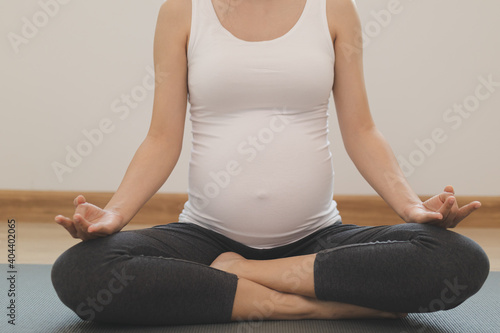 Calm pose young asian pregnant woman practice yoga in the lotus position for pregnant to meditation and exercise on mat for wellbeing while rest at home.